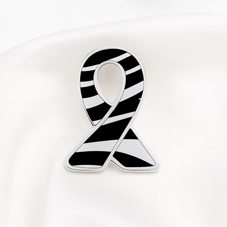 May include: A silver-toned ribbon-shaped pin with a black and white striped pattern. The pin is set against a white background, highlighting its design. The ribbon design is a symbol of awareness.