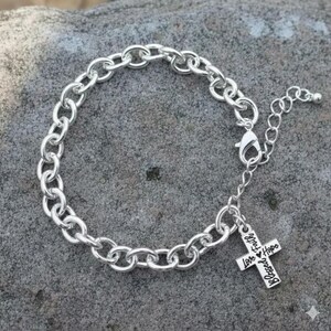 May include: Silver-toned chain bracelet with a cross charm. The bracelet features a series of oval links and an adjustable chain. The cross charm is engraved with the words "Love, Faith, Hope, Blessed".