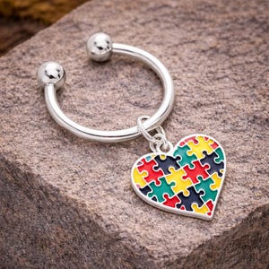 May include: A silver keychain with a heart-shaped charm. The charm is a colorful jigsaw puzzle design with red, yellow, green, and blue pieces. The keychain has a circular design with two small silver balls on each end.