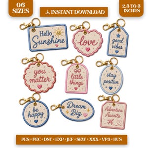 May include: A collection of eight embroidered keychains in various shapes including rectangles, circles, ovals, and hearts. Each features phrases like Hello Sunshine, love, good vibes, you matter, little things, stay positive, be happy, Dream Big, and Adventure Awaits.