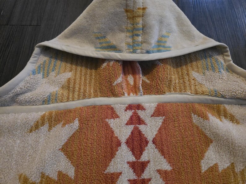 Puede incluir: Una toalla con capucha con un patr&oacute;n geom&eacute;trico en tonos naranja, blanco y azul. La toalla est&aacute; hecha de un material suave y absorbente y tiene una capucha para mayor calidez y comodidad. El dise&ntilde;o presenta un patr&oacute;n repetido de diamantes y tri&aacute;ngulos.