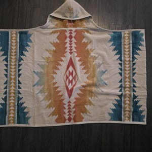 Puede incluir: Una toalla de playa con capucha con un patr&oacute;n geom&eacute;trico en tonos beige, naranja, turquesa y rojo. El dise&ntilde;o presenta una forma de diamante central y rayas verticales con acentos triangulares. La toalla est&aacute; hecha de material suave.