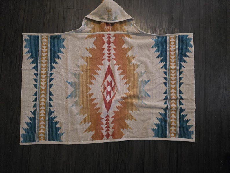 Puede incluir: Una toalla de playa con capucha con un patr&oacute;n geom&eacute;trico en tonos beige, naranja, turquesa y rojo. El dise&ntilde;o presenta una forma de diamante central y rayas verticales con acentos triangulares. La toalla est&aacute; hecha de material suave.