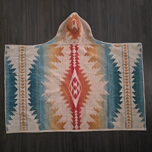 Puede incluir: Una toalla con capucha con un dise&ntilde;o de inspiraci&oacute;n suroeste. La toalla presenta una base color crema con rayas verticales en turquesa, naranja y amarillo. Un patr&oacute;n de diamante central en rojo y naranja a&ntilde;ade un punto focal. La capucha refleja el dise&ntilde;o.