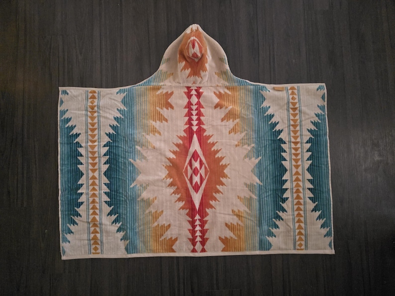 Puede incluir: Una toalla con capucha con un dise&ntilde;o de inspiraci&oacute;n suroeste. La toalla presenta una base color crema con rayas verticales en turquesa, naranja y amarillo. Un patr&oacute;n de diamante central en rojo y naranja a&ntilde;ade un punto focal. La capucha refleja el dise&ntilde;o.