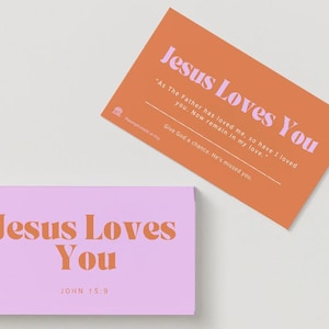 May include: Two rectangular cards. One is orange with light pink text reading "Jesus Loves You," "As The Father has loved me, so have I loved you. Now remain in my love," and "Give God a chance. He's missed you." The other is light pink with orange text reading "Jesus Loves You" and "JOHN 15:9."