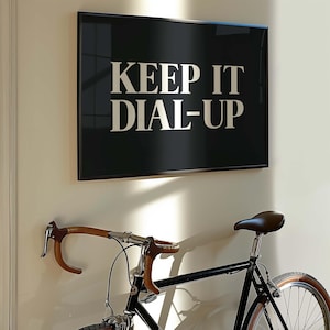 May include: A black framed wall art piece with the text "KEEP IT DIAL-UP" in white lettering hangs above a black bicycle. The bicycle has brown handlebars and a brown leather seat.