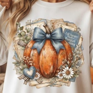 May include: A white sweatshirt featuring a graphic of an orange pumpkin adorned with a large blue bow. The design includes vintage book pages, eucalyptus sprigs, white daisies, a blue heart, and a blue sign with the text Fall Sweater Weather Pumpkin.