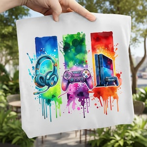 May include: White tote bag featuring a colorful watercolor design of gaming accessories. The design includes a blue headset, a purple controller, and a game console with a controller. The background has splashes of blue, green, and red.
