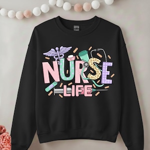 Puede incluir: Sudadera negra con las palabras "NURSE LIFE" en colores pastel. El diseño incluye símbolos médicos como un caduceo, un estetoscopio, una jeringa y una taza de café. Las letras tienen una variedad de patrones y texturas.