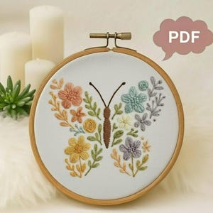 May include: A round embroidery hoop featuring a butterfly design. The butterfly is composed of colorful embroidered flowers in shades of peach, yellow, blue, and purple. The text "PDF" is in a pink speech bubble.