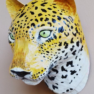 May include: A paper mache leopard head sculpture with a yellow and black spotted pattern. The sculpture has green eyes and a white muzzle.