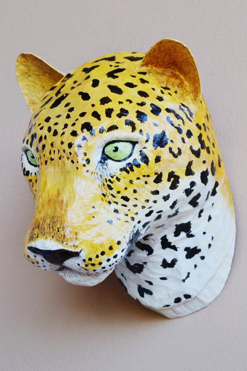 May include: A paper mache leopard head sculpture with a yellow and black spotted pattern. The sculpture has green eyes and a white muzzle.