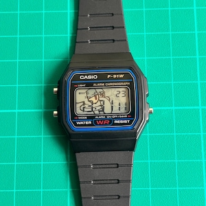 May include: Black Casio F-91W digital watch with a rectangular face and black resin band. The watch face displays the time, date, and other functions. The watch has a blue and black border with the Casio logo and model number.