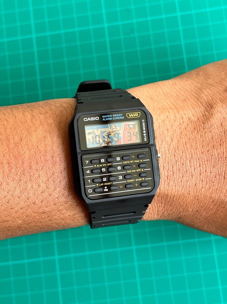 May include: Black Casio digital watch with a rectangular face and multiple buttons. The watch displays the time and has the text "WATER RESIST ALARM CHRONO" and "WR". The watch is on a wrist.