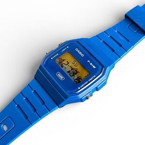 May include: A vibrant blue Casio F-91W digital watch. The watch features a rectangular face with a digital display showing the time. The watchband and case are a matching bright blue. The watch has buttons for mode, light, and alarm functions.