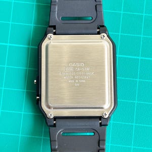 May include: Close-up of a Casio CA-53W digital watch. The watch has a black resin strap and a stainless steel back. The back of the watch has the Casio logo and model information, including "WATER RESISTANT" and "MADE IN CHINA".