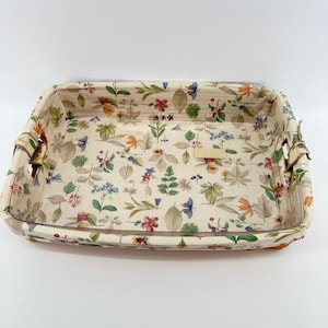 May include: Rectangular serving tray with a floral pattern. The tray features a cream-colored background with a repeating pattern of colorful flowers and leaves. The edges are a light brown color, and the tray has handles on each side.