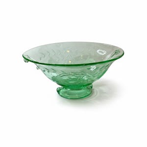 May include: A translucent light green glass bowl featuring a wide, flared rim and a pedestal base. The exterior surface of the bowl is decorated with an etched pattern of repeating leaf motifs that wrap around the entire circumference of the vessel.