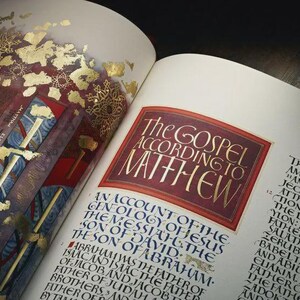 Peut inclure: Livre ouvert avec des pages de calligraphie ornée. Le texte "The Gospel According to Matthew" est affiché en lettres dorées sur un fond bordeaux. Des accents de feuilles d'or et des éléments décoratifs sont visibles.