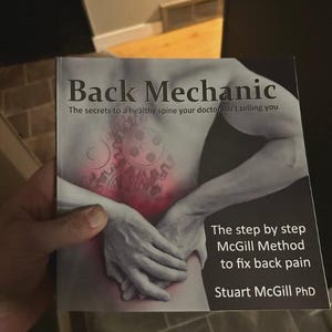 以下が含まれることがあります： 「Back Mechanic」というタイトルの本で、「あなたの医者が教えてくれない健康な脊椎の秘密」というサブタイトルが付いています。表紙には、歯車と「The step by step McGill Method to fix back pain」というテキストが描かれた背中のイラストが描かれています。