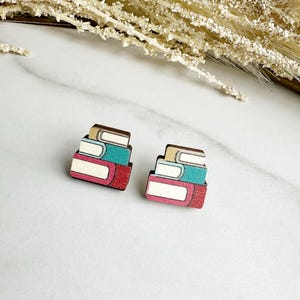 May include: A pair of wooden earrings shaped like a stack of books. The books are painted in shades of red, blue, and white.