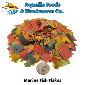 May include: A pile of colorful marine fish flakes, with red, yellow, green, and gray hues. The image includes a US quarter for size reference. The text at the top reads "Aquatic Foods & Blackworm Co." and the text at the bottom reads "Marine Fish Flakes."