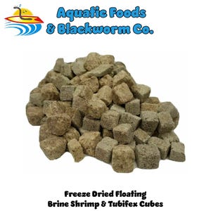 May include: A pile of freeze-dried floating brine shrimp and tubifex cubes. The cubes are a mix of light and medium brown, with a slightly rough texture. The image includes the text "Aquatic Foods & Blackworm Co."