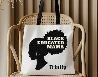 Könnte beinhalten: Weiße Tragetasche mit schwarzen Griffen. Sie zeigt eine schwarze Silhouette eines Frauenprofils, den Text "BLACK EDUCATED MAMA" und den Namen "Trinity". Die Tasche liegt auf einem Korbstuhl.
