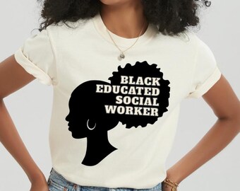 Könnte beinhalten: Cremefarbenes T-Shirt mit schwarzer Silhouette eines Frauenprofils, Afro und Creolen. Der Text "BLACK EDUCATED SOCIAL WORKER" ist schwarz aufgedruckt. Das Model trägt blaue Jeansshorts.