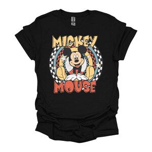 May include: Black t-shirt featuring a retro design of Mickey Mouse. The graphic includes the words "Mickey Mouse" in yellow and red, with Mickey in the center, surrounded by a rainbow and stars.