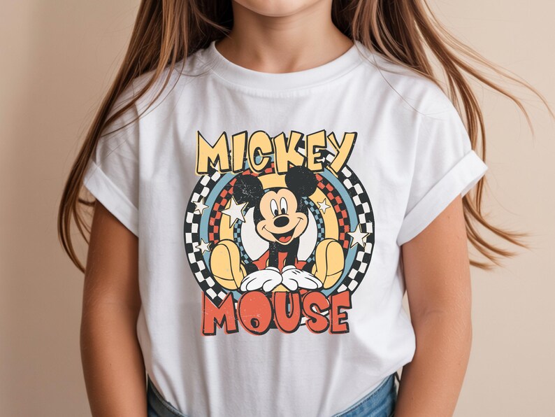 May include: White t-shirt featuring a retro Mickey Mouse graphic. The design includes the words "Mickey Mouse" in a vintage font, with Mickey in the center. The graphic has a circular design with stars and a checkered pattern.