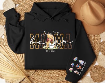 May include: Black hoodie featuring a Winnie the Pooh design with the words "Mama Bear" and "EST. 2021". The sleeve has a graphic of characters with balloons and names. The hoodie is made of a soft material.