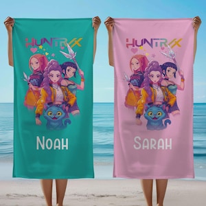 May include: Two beach towels, one teal and one pink, are held up. Each features a colorful anime-style illustration of three girls and a blue cat. The teal towel says "NOAH" and the pink towel says "SARAH" in white text. The towels have the text "HUNTRAX".