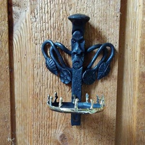 May include: A black metal wall mounted candle holder with a stylized face and a gold-colored tray.