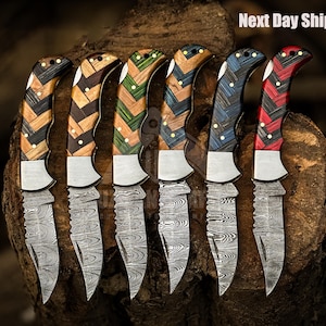 May include: Six folding knives with patterned wooden handles in various colors, including brown, green, blue, and red. The blades have a unique etched design. The text "Next Day Shipping" is visible in the top right corner.