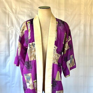 Könnte beinhalten: Ein lilafarbener Seidenkimono mit cremefarbenem Kragen und einem Muster aus schwarzem Bambus und japanischen Schriftzeichen. Der Kimono befindet sich auf einem weißen Hintergrund.