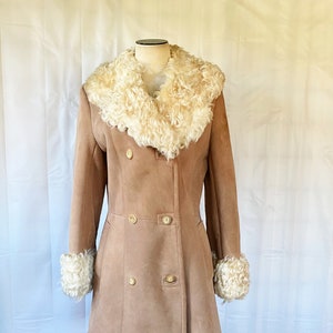 May include: A tan suede coat with a large white faux fur collar and cuffs. The coat has a double breasted closure with gold buttons.