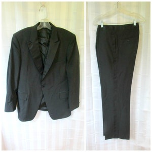 Op de afbeelding: Een zwart smokingpak met een enkelknoops jasje en bijpassende broek. Het jasje heeft een shawlkraag en satijnen bies. De broek heeft een enkele vouw aan de voorkant en een satijnen streep langs de zijkant.