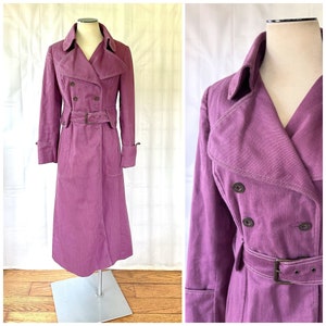 May include: A long, double-breasted purple trench coat with a belt. The coat has a pointed collar and flap pockets.