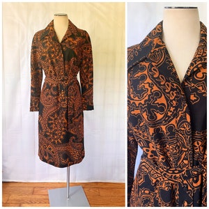 Könnte beinhalten: Ein langärmeliges Kleid mit Paisley-Muster in Orange- und Schwarztönen. Das Kleid hat einen Kragen, einen Knopfleistenverschluss und einen Gürtel.
