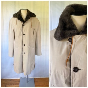 May include: A beige long coat with a brown faux fur collar and brown leather accents. The coat has a button closure and two pockets.