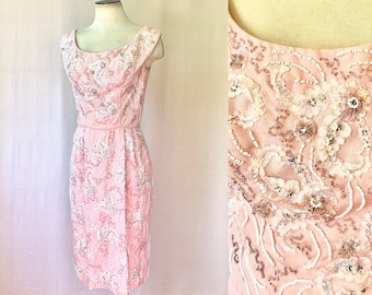 May include: A pink sleeveless dress with a fitted silhouette and intricate white and silver beading and sequins. The dress has a scoop neckline and a back zipper closure.