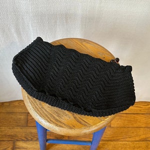 May include: Black knitted bag with a woven pattern. The bag has a brown bead accent.