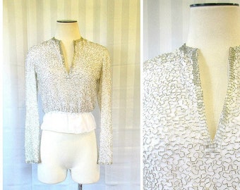 May include: A white, long-sleeved top with a V-neck and a delicate, beaded design. The top is made of a sheer fabric and has a fitted silhouette.