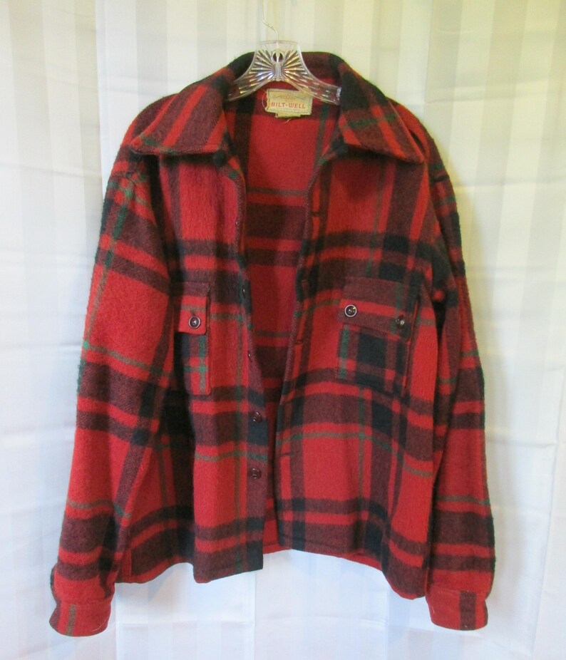 May include: Red, black, and green plaid flannel shirt with a button-up front and two flap pockets. The shirt has a "Milt-Dell" label.