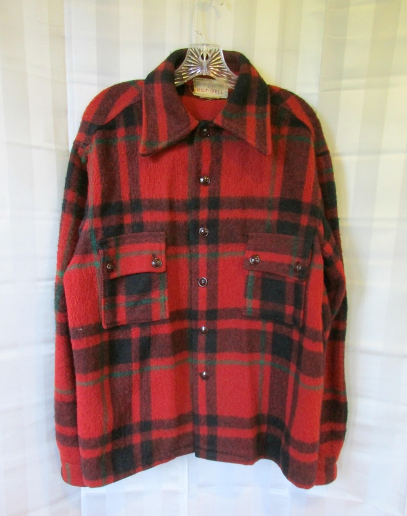 May include: Red, black, and green plaid flannel shirt with a button-up front and two flap pockets. The shirt has a "WOLF-DELL" label.