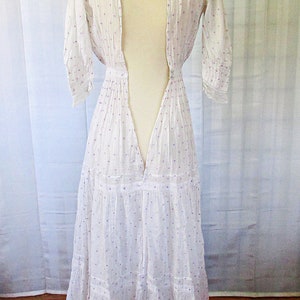May include: A white cotton dress with a purple polka dot pattern. The dress has a deep V-neckline and a tiered skirt. The dress is on a white mannequin.