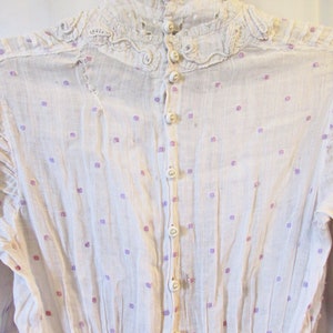 May include: White cotton blouse with a high lace collar and a row of pearl buttons down the back. The blouse has a small purple and white polka dot pattern.