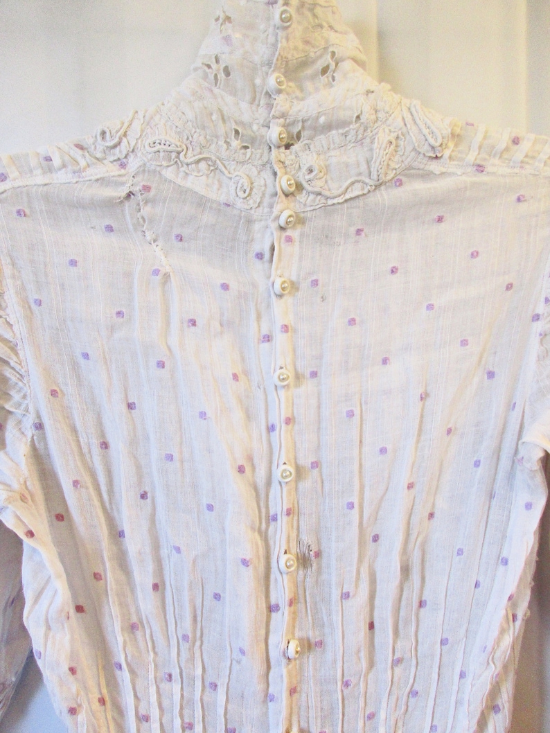 May include: White cotton blouse with a high lace collar and a row of pearl buttons down the back. The blouse has a small purple and white polka dot pattern.